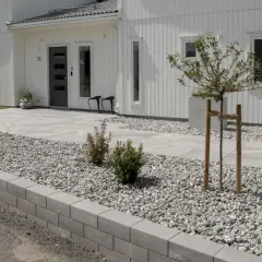 Inspiration rabatt med sten. Ett modernt hus med vit träfasad, grå stenläggning och en rabatt fylld med grå stenar och små buskar.