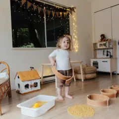 Dziecko bawi się w pokoju inspirowanym 10 zasadami Montessori. Drewniane zabawki, domek i kuchnia zachęcają do samodzielnej nauki.