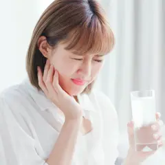 Donna con espressione sofferente, tiene un bicchiere d'acqua, soffre di ipersensibilità dentale.
