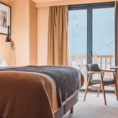 Chambre d'hôtel avec lit douillet, vue sur les montagnes enneigées et télécabines.
