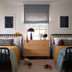 Twin beds with colorful quilts and star charts create fun boys bedroom ideas. A wooden dresser holds globes and a lamp.