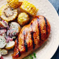 Un délicieux poulet grillé au sirop d'érable, servi avec une salade de pommes de terre crémeuse et des épis de maïs rôtis.