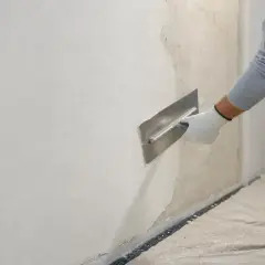 Lavoratore con spatola effettua rasatura muro esterno con rete, creando una finitura liscia e uniforme.