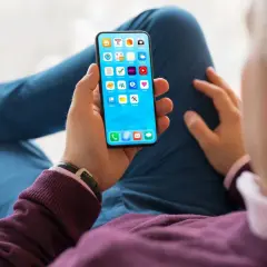 Dłoń trzyma smartfon z ikonami aplikacji. Szybkość ładowania telefonu zależy od wielu czynników, np. ładowarki i stanu baterii.