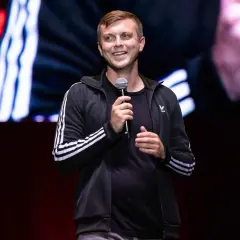 Uśmiechnięty Krajewski na scenie, trzyma mikrofon. Jego stand up rozgrzewa publiczność.