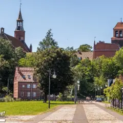 Tczew atrakcje: zabytkowy kościół, urokliwe kamieniczki i zielony park. Spacerowicze cieszą się słonecznym dniem.