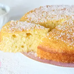 Una soffice torta al cocco, cosparsa di scaglie bianche, con una fetta tagliata che ne rivela l'interno profumato.
