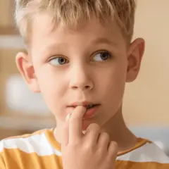 Chłopiec z blond włosami i niebieskimi oczami, z palcem w ustach, może być przykładem, jak objawy spektrum autyzmu mogą się manifestować.