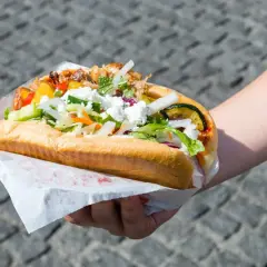 Kebab z kurczakiem w bułce z warzywami i serem feta, trzymany w dłoni.