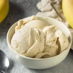 Un cremoso helado de plátano en un tazón blanco, con plátanos amarillos frescos al lado.