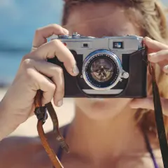 Kobieta z aparatem na plaży, idealna inspiracja do stworzenia własnych darmowych akcji do Photoshop.