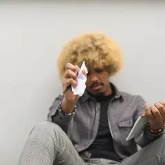 Mężczyzna z afro włosami siedzi, trzymając ołówek i zmiętą kartkę papieru.
