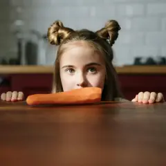Bambina con acconciatura a ciambella guarda una carota, forse un caso di neofobia alimentare.