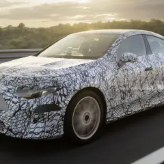 Zamaskowany prototypowy Mercedes CLA 2025 na drodze, z widokiem na zachodzące słońce i drzewa w tle.