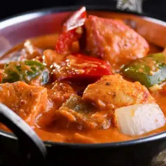 Delicioso pollo al curry con leche de coco, pimientos y cebolla en un cuenco metálico.