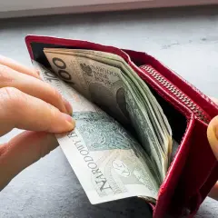 Ręce wkładają pieniądze do czerwonego portfela. To może być symbol wsparcia finansowego, jak zus renta rodzinna po mężu.