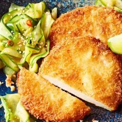Knuspriges Kohlrabi-Schnitzel mit Gurkensalat und Limettenspalten auf einem blauen Teller.