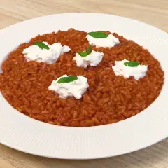 Un invitante risotto al pomodoro, arricchito da ciuffi di ricotta fresca e basilico, pronto per essere gustato.
