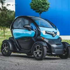 Niebiesko-czarny Renault Twizy stoi na drodze przed niebieskim budynkiem.