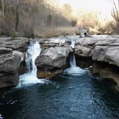 Cascada en la riera del Palau, con rocas erosionadas y vegetación de ribera. El agua cae formando remolinos.