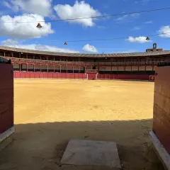 La plaza de toros de Toro, con su arena dorada y gradas rojas, espera bajo un cielo azul con nubes.