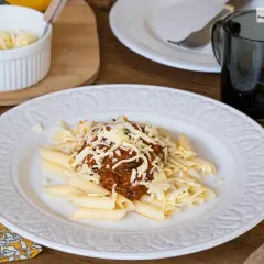 Macarrones con carne picada, cubiertos de queso rallado, servidos en un plato blanco con un diseño floral.