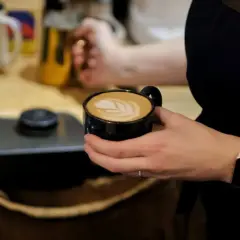 Barista trzyma kubek z flat white, ozdobiony latte art. Pyszna kawa, której kcal nie są wysokie.