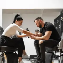 Barber w czarnym t-shircie i podartych jeansach siedzi na fotelu, trzymając dłoń klientki. Zastanawia się, ile zarabia barber.