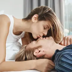 Coppia che si bacia a letto, un momento intimo e tenero che celebra la ritrovata connessione dopo il parto.