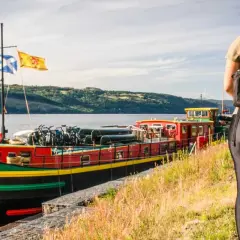 A cyclist pauses by a colorful barge loaded with bikes, ready for an adventure on the water.
