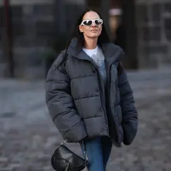 Frau mit Daunenjacke, die sie ohne Trockner wäscht, trägt weiße Sonnenbrille und schwarze Tasche.
