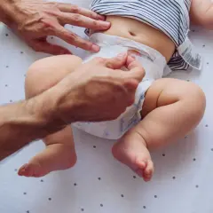 Rączki taty zmieniają pieluszkę, na której widać śluz w kupie niemowlaka.
