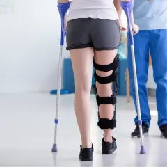 Rehabilitacja po złamaniu nogi: pacjentka w ortezie i z kulami ćwiczy pod okiem fizjoterapeuty.