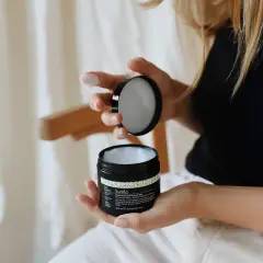 Kobieta z blond włosami kręconymi otwiera słoiczek z maską do włosów.