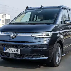 Ciemny Volkswagen California w ruchu drogowym. Sprawdź aktualną volkswagen california cena i planuj podróże!