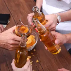 Przyjaciele wznoszą toast butelkami piwa i kieliszkiem, przypominając o procesie, jak powstaje etanol.