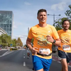 Dwóch biegaczy w pomarańczowych koszulkach na ulicach Warszawy podczas maratonu. Czy to już 42 maraton ile km?