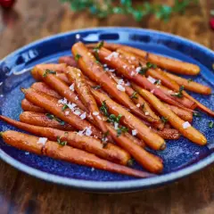 Zanahorias al horno, tiernas y doradas, espolvoreadas con sal marina y hierbas frescas, servidas en un plato azul sobre una mesa de madera.