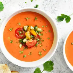 Två skålar med krämig gazpacho, toppad med färska tomater, gurka och örter. Perfekt för ett lätt sommarmål.