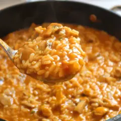 Cuchara sirviendo arroz caldoso con pollo y champiñones, humeante y apetitoso, de una sartén.