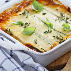 Pasticcio di zucchine appena sfornato, dorato e filante, guarnito con basilico fresco e timo.