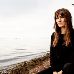 Malin Wollin sitter vid en stenig strand med havet i bakgrunden.