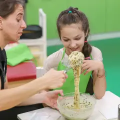 Dziecko z uśmiechem miesza masę, a terapeutka wspiera je w ćwiczeniach ręki.