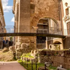 Antiche rovine nel ghetto ebraico di Roma, cosa vedere: un ponte moderno attraversa resti di colonne e mura di mattoni.