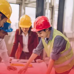 Pracownik budowlany w kasku i kamizelce odblaskowej analizuje plany z zespołem.