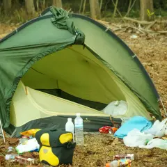 Zielony namiot VAUDE rozbity na leśnej polanie, wokół śmieci. Jaki namiot, taki biwak.