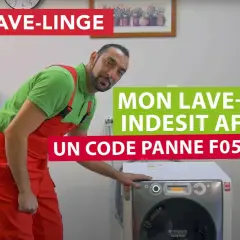 Un homme en salopette rouge devant un lave-linge Indesit 9 kg qui affiche un code panne F05.