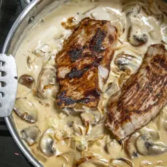 Dwa kawałki grillowanego mięsa w kremowym sosie pieczarkowym Magdy Gessler, gotowe do podania.