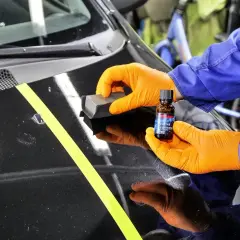Odtłuszczanie lakieru samochodowego przed nałożeniem powłoki ceramicznej. Pomarańczowe rękawiczki, aplikator i buteleczka z produktem.