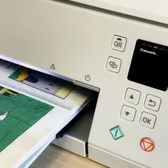 Drukarka drukuje komiks. Ekran pokazuje "Drukowanie...", a papier z rysunkami wychodzi z drukarki. To dobry sposób, jak drukowac dwustronnie.